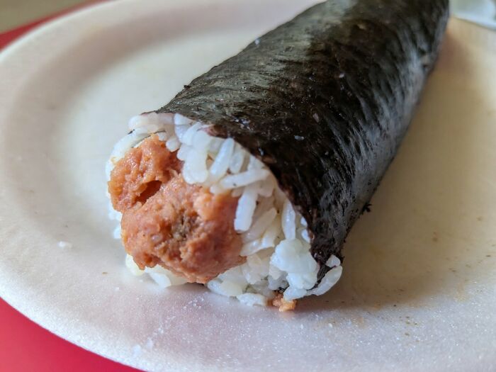 Close-up of a hand roll with unappetizing filling, featuring rice and seaweed in a disgusting food pic.