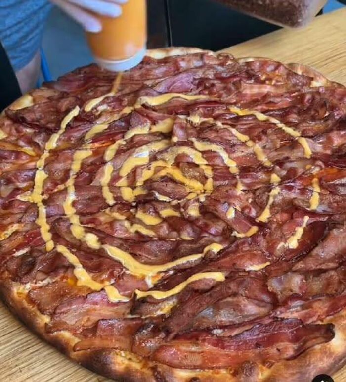 Bacon pizza topped with a spiral of orange sauce being drizzled, featured in disgusting food pics that might ruin appetite.
