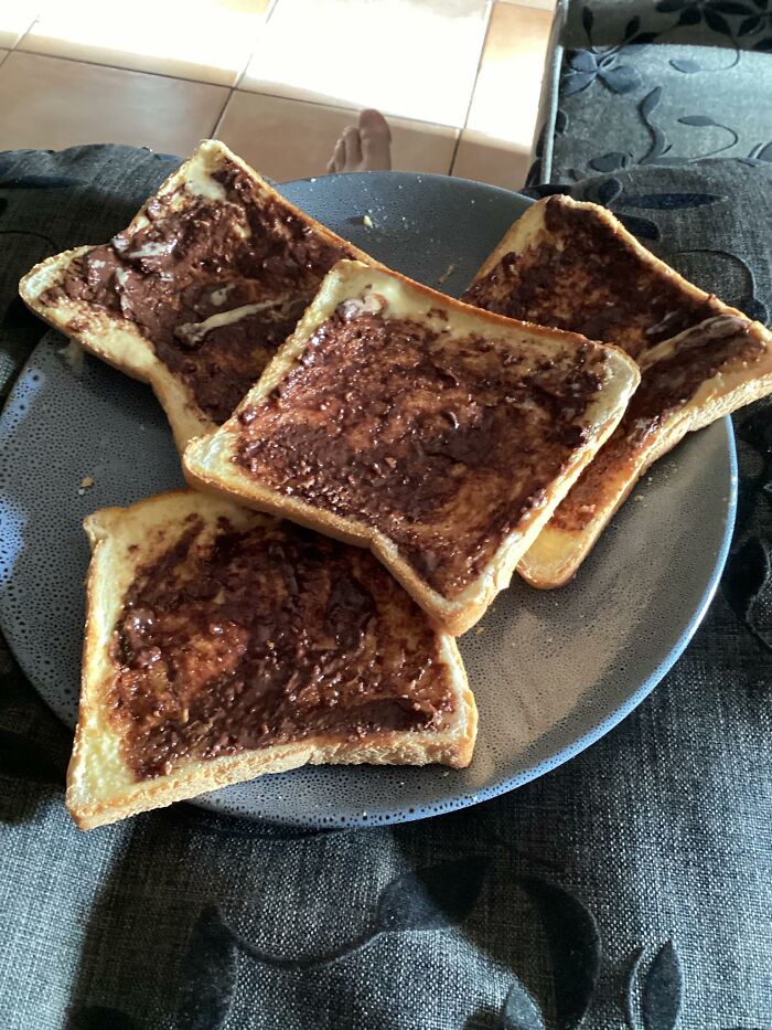 Close-up of four slices of toast with unevenly spread chocolate topping on a plate, showing unappetizing food texture in disgusting food pics.