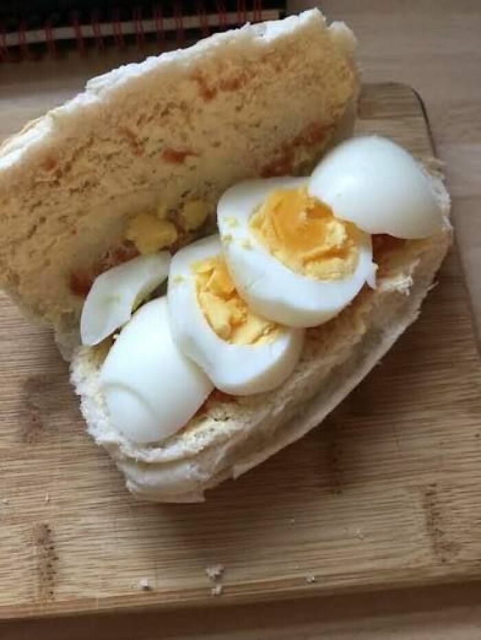 Boiled egg sandwich on plain bread, a disgusting food pic that might ruin your appetite on a wooden cutting board.