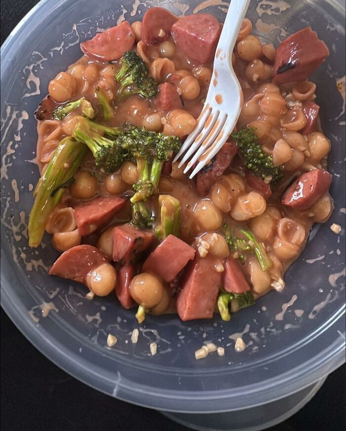 Plastic container with unappetizing mixture of broccoli, sausage pieces, pasta shells, and a sauce, showcasing disgusting food pics.