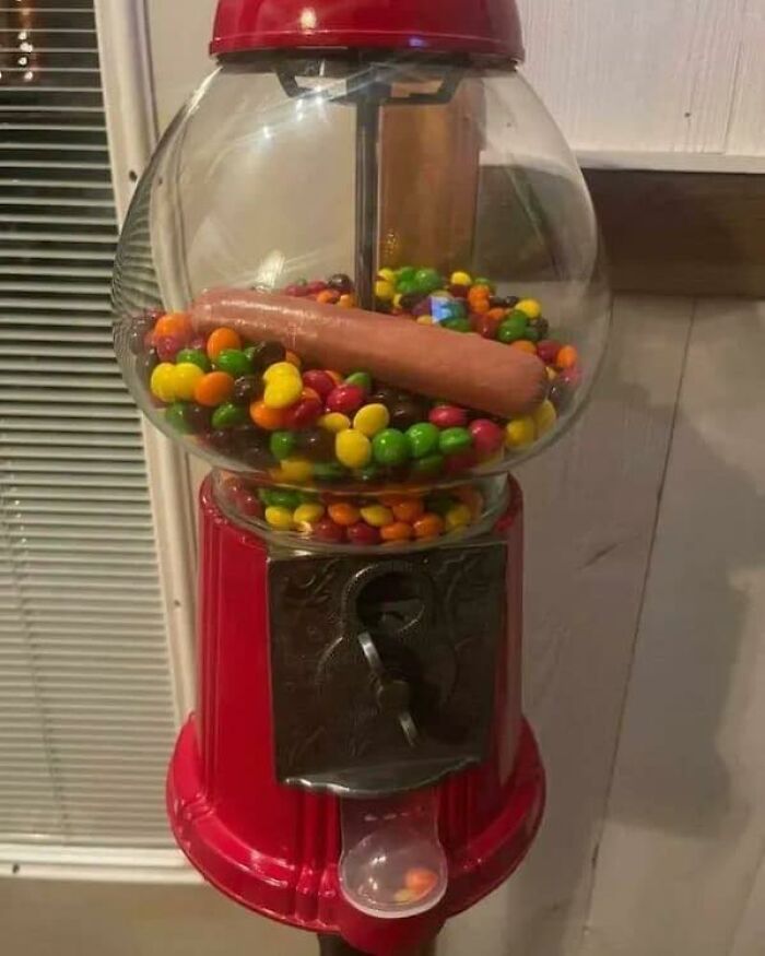 Candy dispenser filled with colorful candy and a hot dog inside, a disgusting food pic that might ruin appetite.