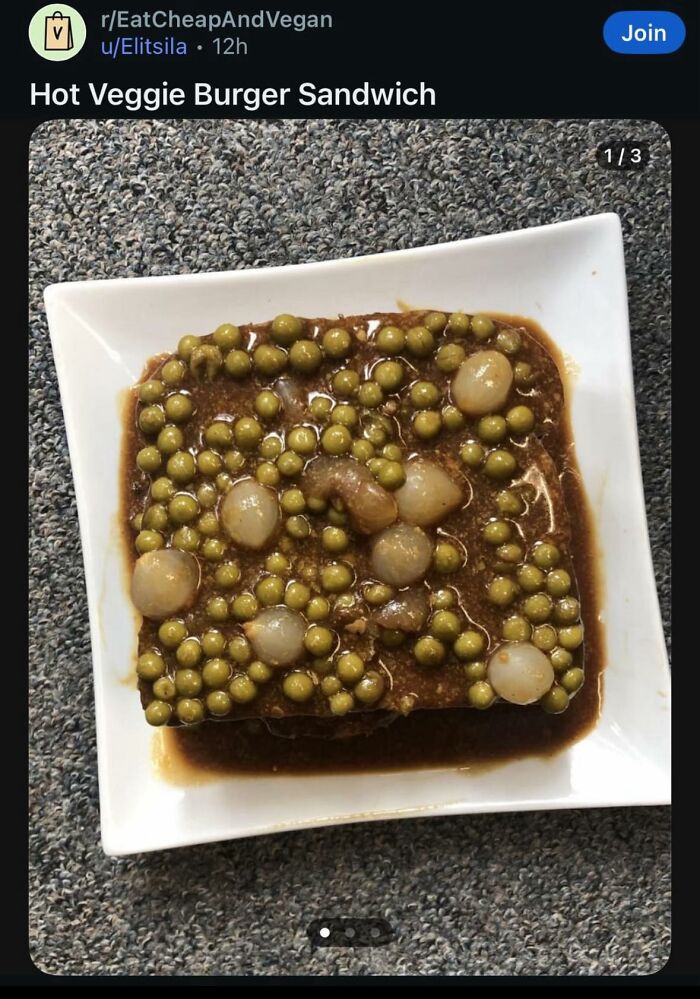 Open-faced sandwich covered with green peas and onions in a brown sauce on a white plate, a disgusting food pic.
