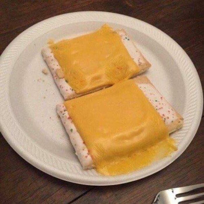 Frosted pastries topped with melted cheese on a white disposable plate, a disgusting food pic that might ruin appetite.
