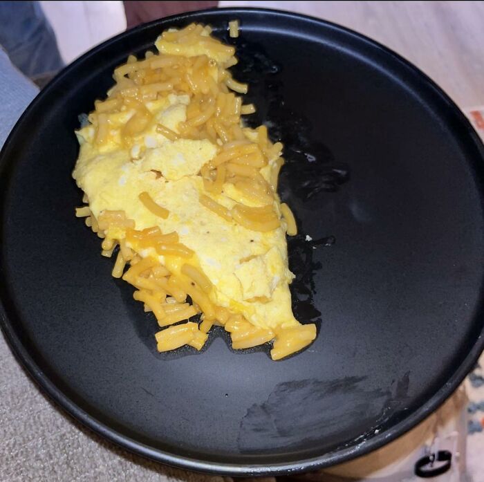 Partially melted and congealed cheese on a broken omelet on a black plate, depicting disgusting food pics.