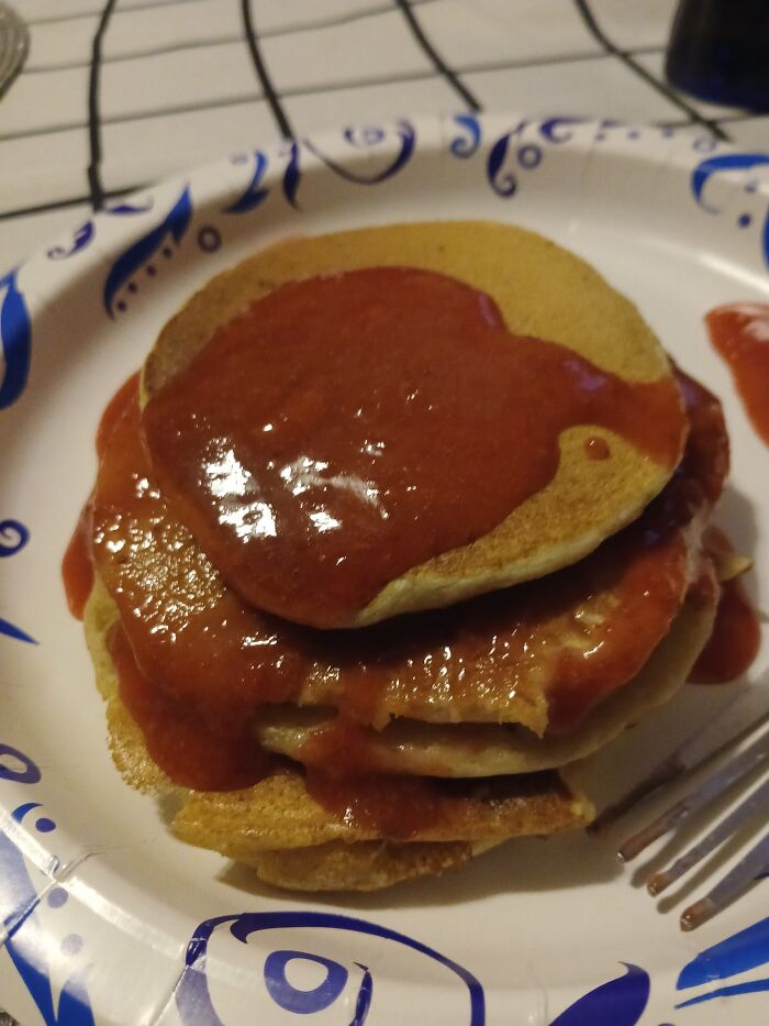Stack of pancakes covered in an unappetizing red sauce on a paper plate in disgusting food pics.