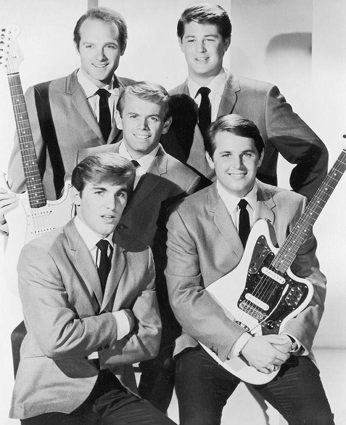 The Beach Boys band members posing with guitars in suits, highlighting legendary co-founder and musical genius tribute.