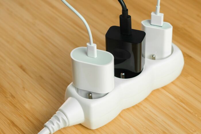 Three phone chargers plugged into a white power strip on a wooden surface, illustrating travel hacks for charging devices.