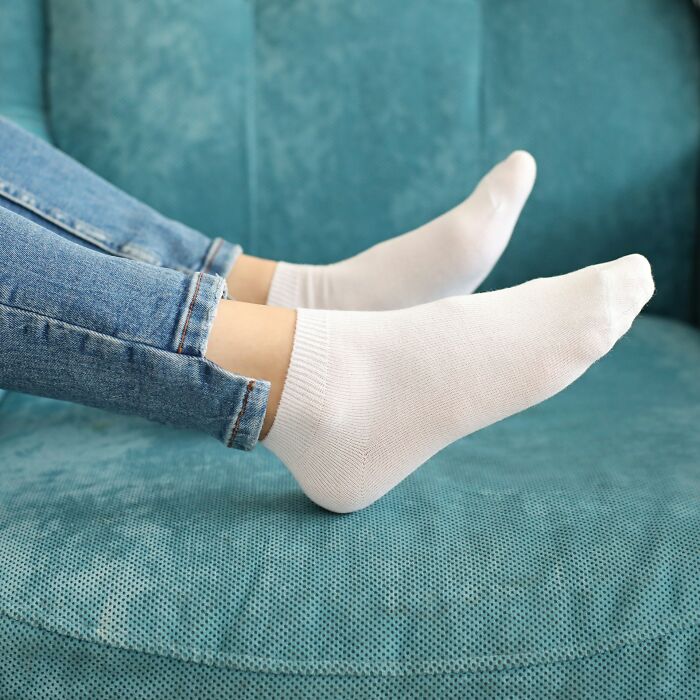Person wearing white socks and blue jeans relaxing on a teal couch, showcasing everyday items under 300 dollars.