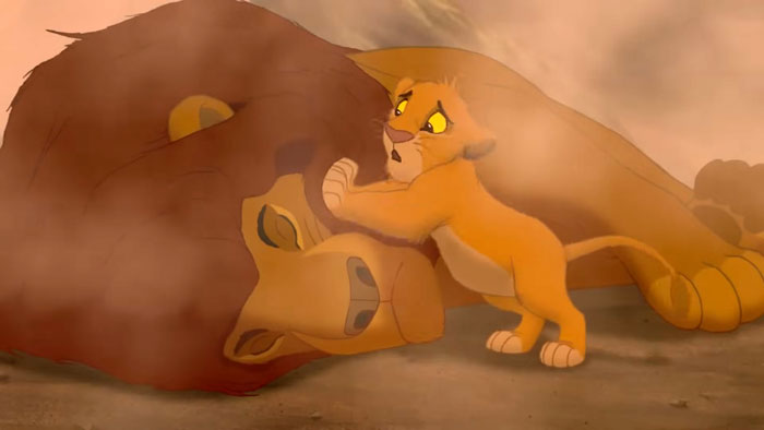 Scene from an animated character death moment showing a lion cub mourning over an adult lion&rsquo;s fallen body.