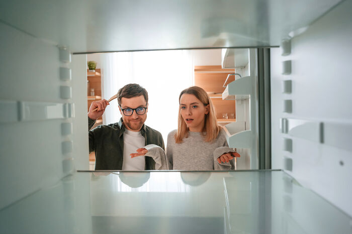 Young couple looking confused and surprised inside an empty fridge, illustrating things learned embarrassingly late.