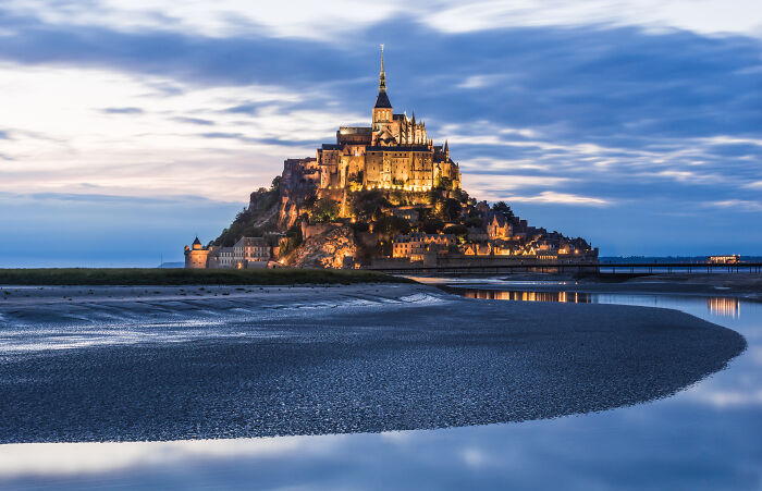 Mont Saint-Michel island and abbey illuminated at dusk, reflecting on calm water, symbolizing things learned embarrassingly late.