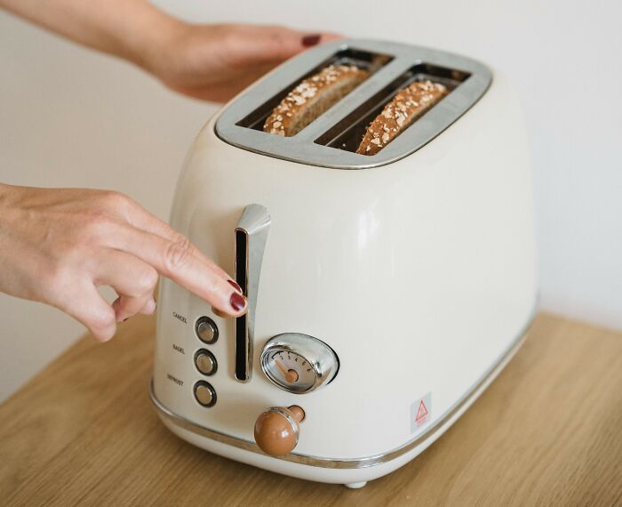 Person adjusting a cream-colored toaster with bread inside, illustrating things learned embarrassingly late.