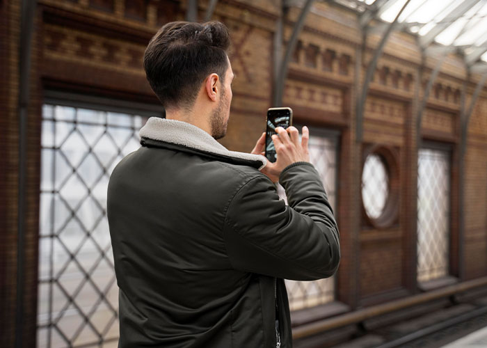 Man in a green jacket using smartphone to take photos, illustrating modern behaviors some people can’t accept today.