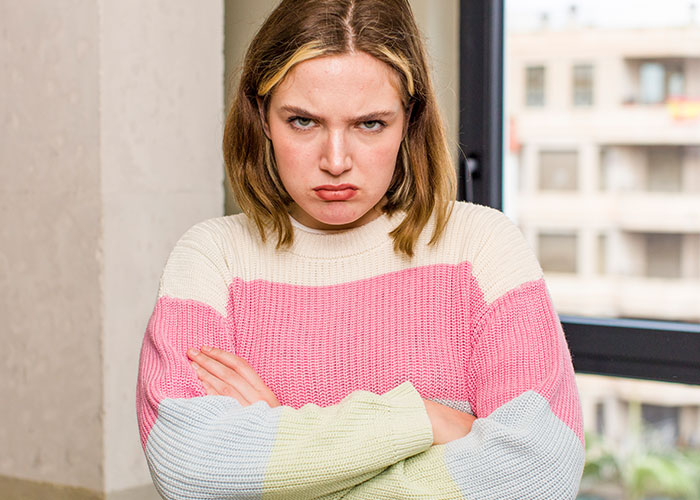 Young woman wearing a colorful sweater with crossed arms, showing frustration with modern behaviors she can’t accept.