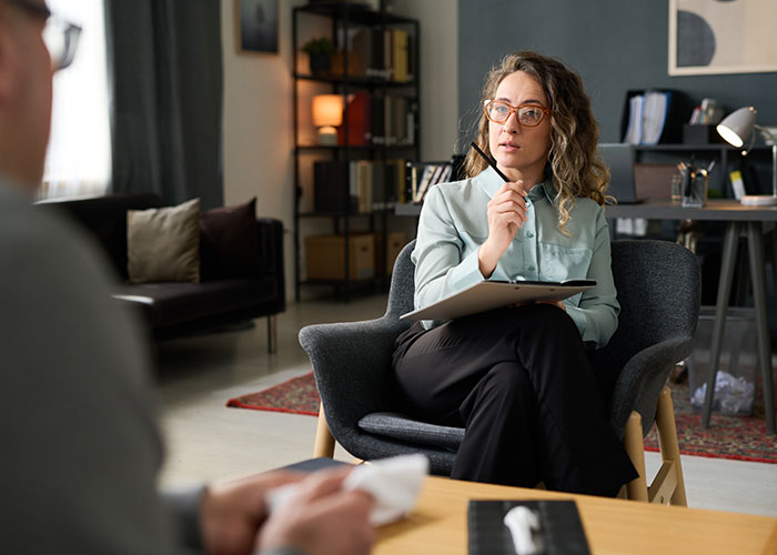 Therapist listening attentively to a client in a modern office, discussing behaviors and generational perspectives.