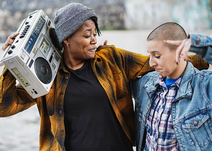 Two friends enjoying music outdoors, showcasing modern behaviors and expressions shaped by how they grew up.