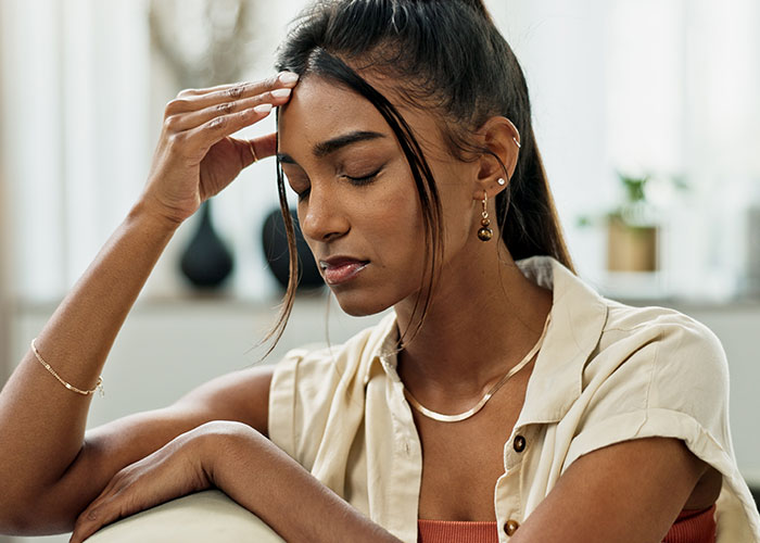Young woman sitting with eyes closed and hand on forehead, reflecting on modern behaviors she can’t accept.
