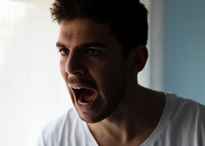 Young man expressing frustration indoors, illustrating modern behaviors some people struggle to accept due to upbringing differences.