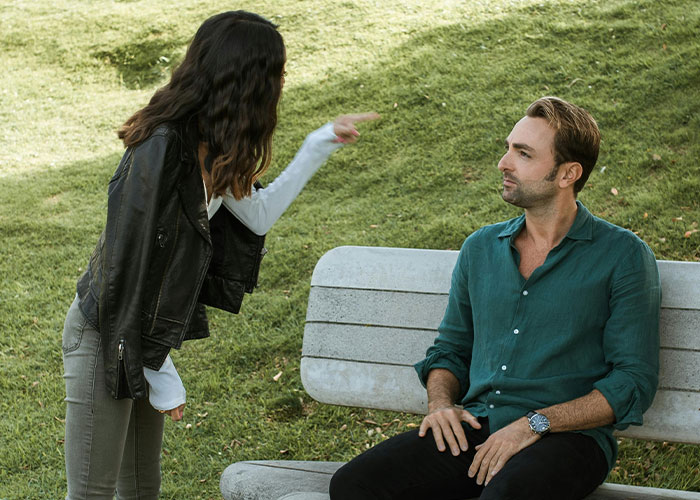 A woman angrily talking to a man sitting on a park bench, illustrating modern behaviors they can’t accept.