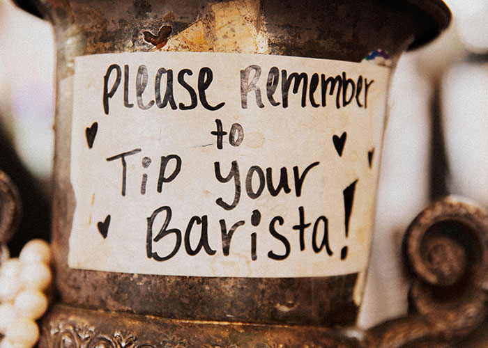 Handwritten note on a rustic metal container reminding customers about tipping, highlighting modern behaviors and tipping etiquette.