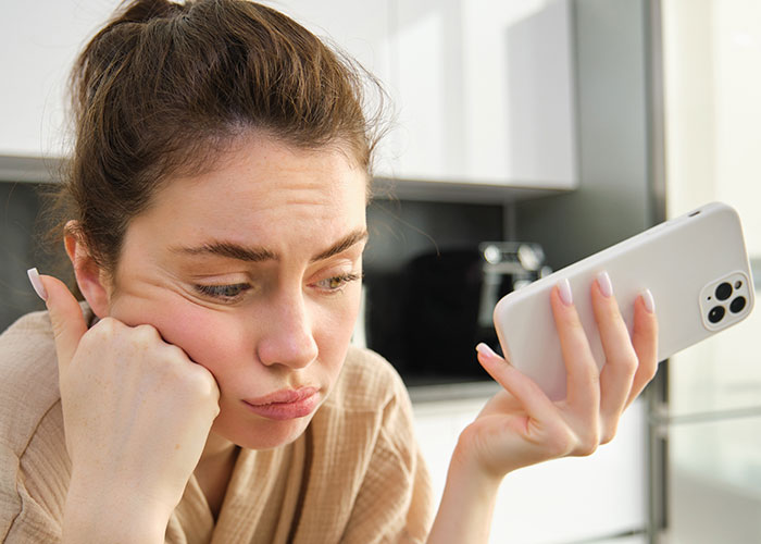 Young woman looking frustrated while holding a smartphone, reflecting on modern behaviors she can’t accept from upbringing