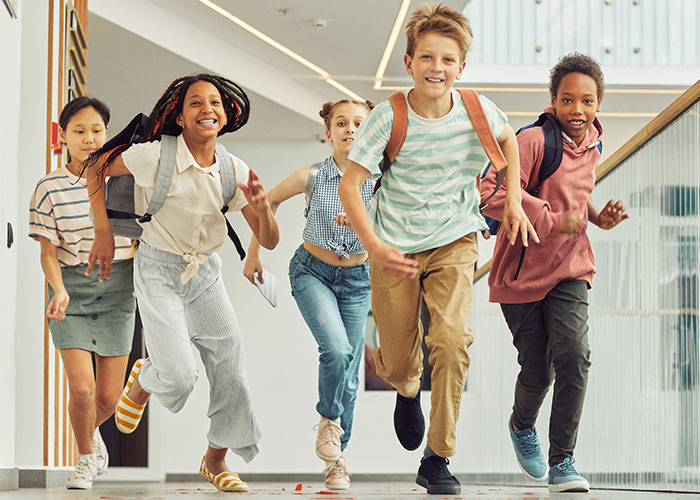 Group of diverse kids with backpacks running happily down a school hallway, reflecting modern behaviors and childhood experiences.