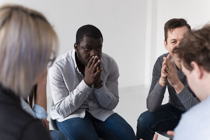 A diverse group in a support circle, focusing on a man showing signs of distress, reflecting dark truths in human behavior.