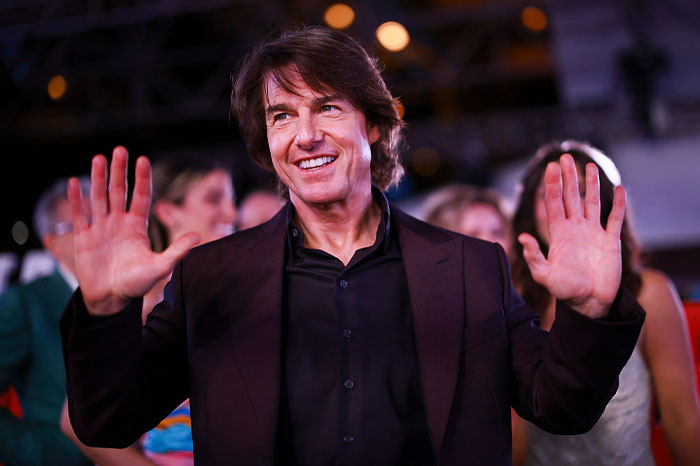 Tom Cruise smiling and raising hands at an event, illustrating his net worth staying sky-high for decades.