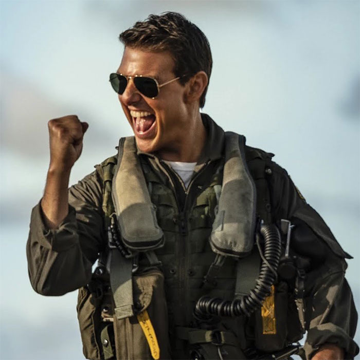Tom Cruise celebrating in aviator sunglasses and flight suit, showcasing the long game of his net worth success.