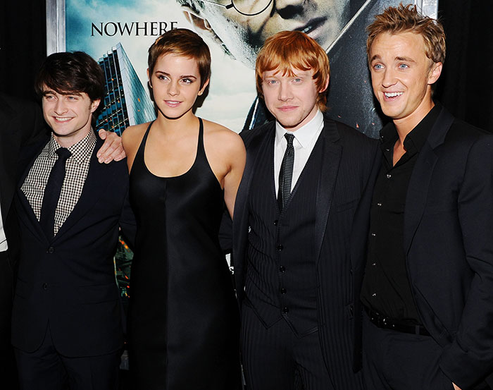 Daniel Radcliffe, Emma Watson, Rupert Grint, and Tom Felton posing together on a red carpet at a Harry Potter event.