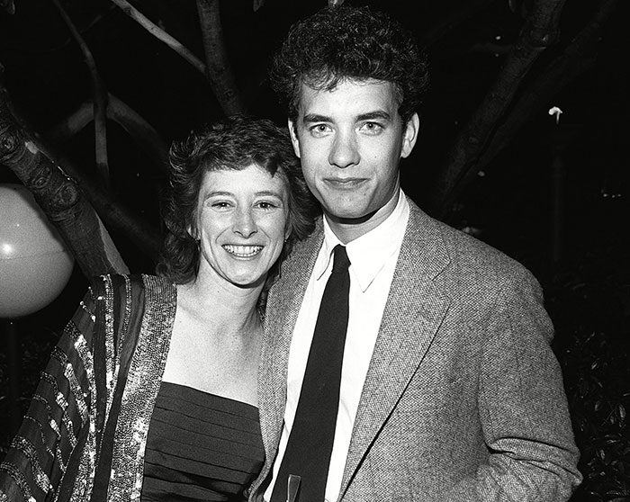 Tom Hanks smiling with a woman at a nighttime event, dressed in vintage formal attire.