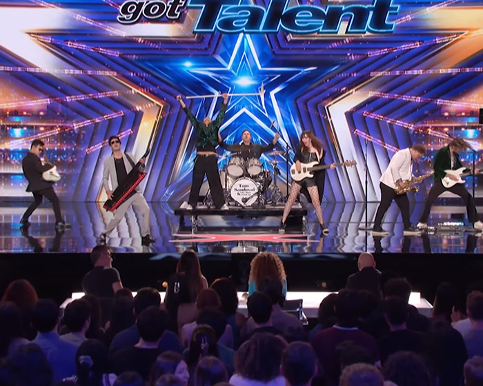 Tom Sandoval performing on America's Got Talent stage with a live band and audience watching the audition.