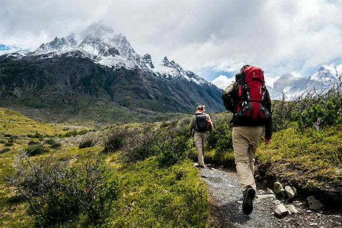 Two hikers with backpacks trekking a mountain trail under cloudy skies, illustrating awkward moments of nice guys turning creepy.
