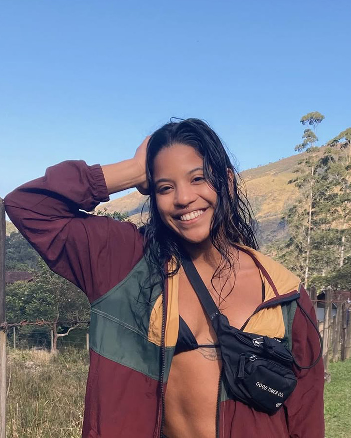 Young tourist smiling outdoors wearing a maroon jacket and black bikini top with hills in the background.