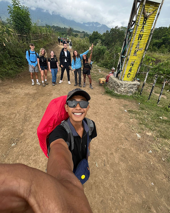 Young tourist taking a selfie with a group on a hiking trail near an active volcano, capturing the moment outdoors.