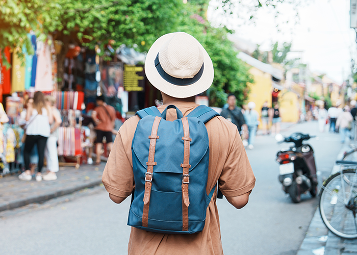 Tourist with backpack and hat walking through busy street near historic site with 2000-year-old statues. Tourist with backpack and hat walking through busy street near historic site with 2000-year-old statues.