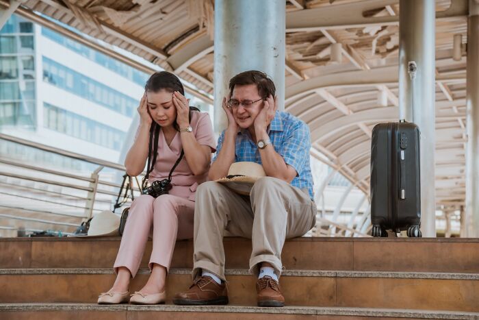 A stressed couple sitting on steps at a travel terminal with luggage, showing frustration during a travel experience.