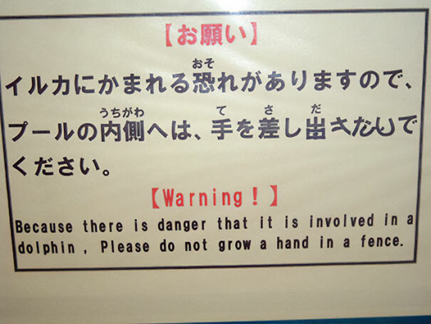 Sign with funny and baffling English translation warning about dolphin danger and not putting hand in pool fence.