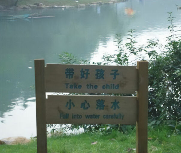 Wooden sign by water with funny English translation errors warning to take the child and avoid falling in water carefully.