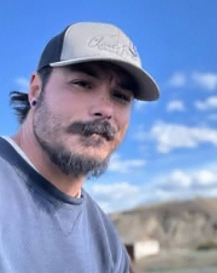 Man wearing a cap outdoors with blue sky, related to bodies of 3 missing sisters found as police hunt for their father.