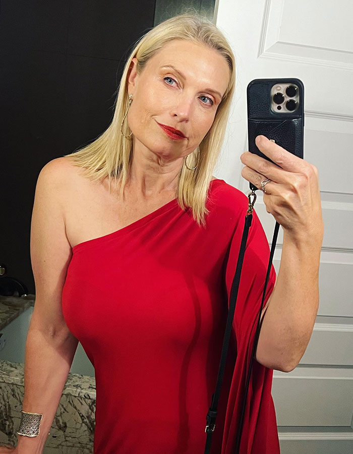 Woman in a red one-shoulder dress taking a selfie, linked to Elon Musk&rsquo;s sister&rsquo;s steamy romance service story.