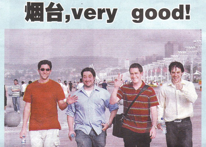 Group of four men walking and smiling on a city promenade, sharing their most unbelievable experiences confidently.