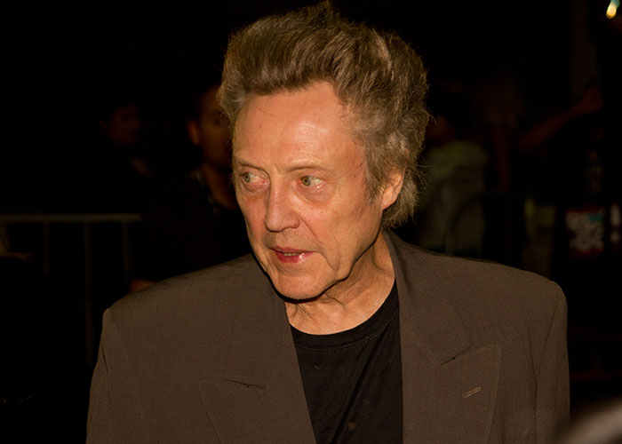 Man with styled hair and a brown blazer sharing an unbelievable experience in a dimly lit setting.