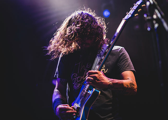 Man with long hair playing electric guitar on stage under purple lighting sharing unbelievable experiences.