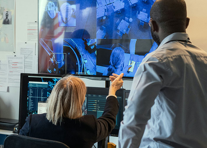 Two professionals examining multiple screens showing surveillance footage and data, sharing unbelievable proven experiences.