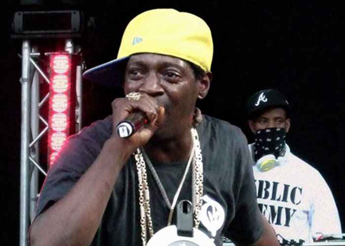 Man wearing a yellow cap and chains performing on stage, sharing unbelievable experiences with a microphone.