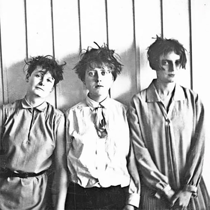 Three women in disheveled clothes with wild hair standing against a wall in a rare historical photo.