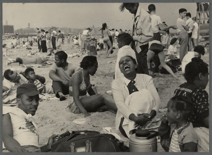 Rare historical photo showing a lively beach scene with diverse groups of people enjoying a sunny day outdoors.