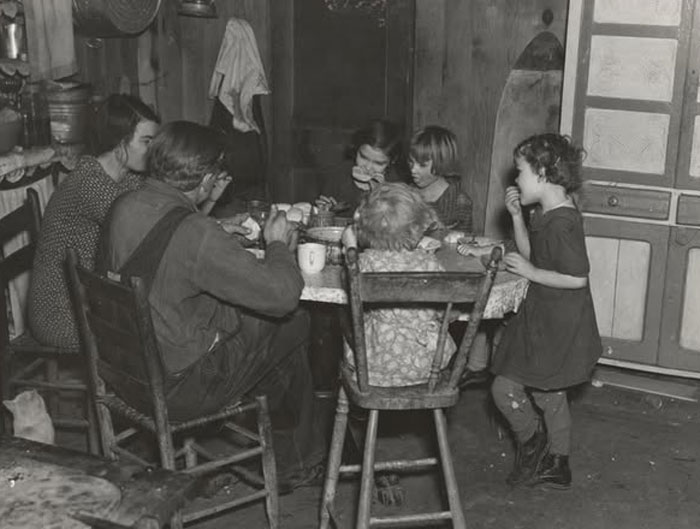 Rare historical photo of a family sharing a meal around a kitchen table in a modest home setting.